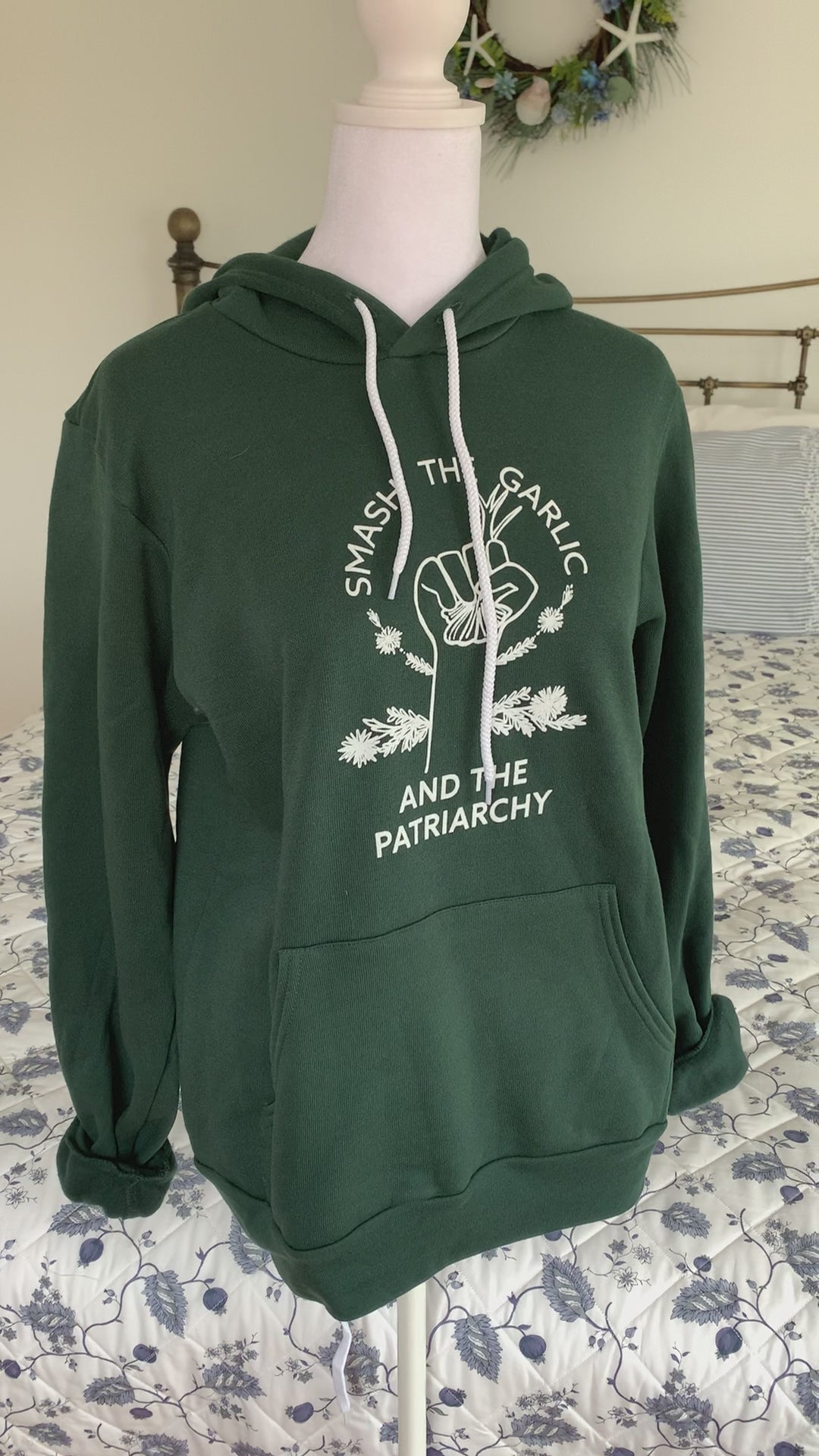 A dark green hoodie that reads "Smash the Garlic and the Patriarchy" hangs on a manikin" 