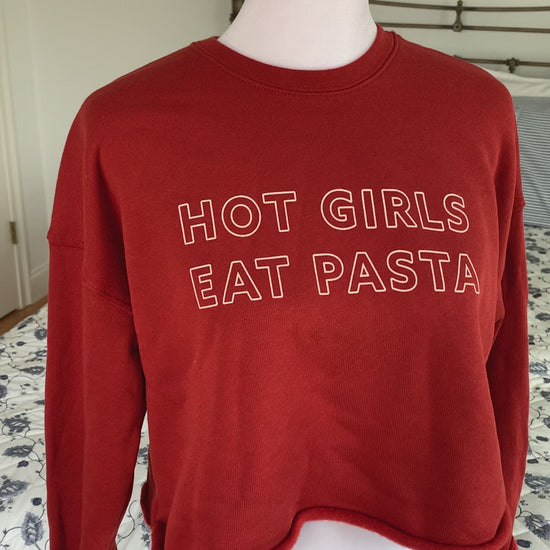 A red cropped sweatshirt that reads "Hot Girls Eat Pasta" hangs on a manikin 