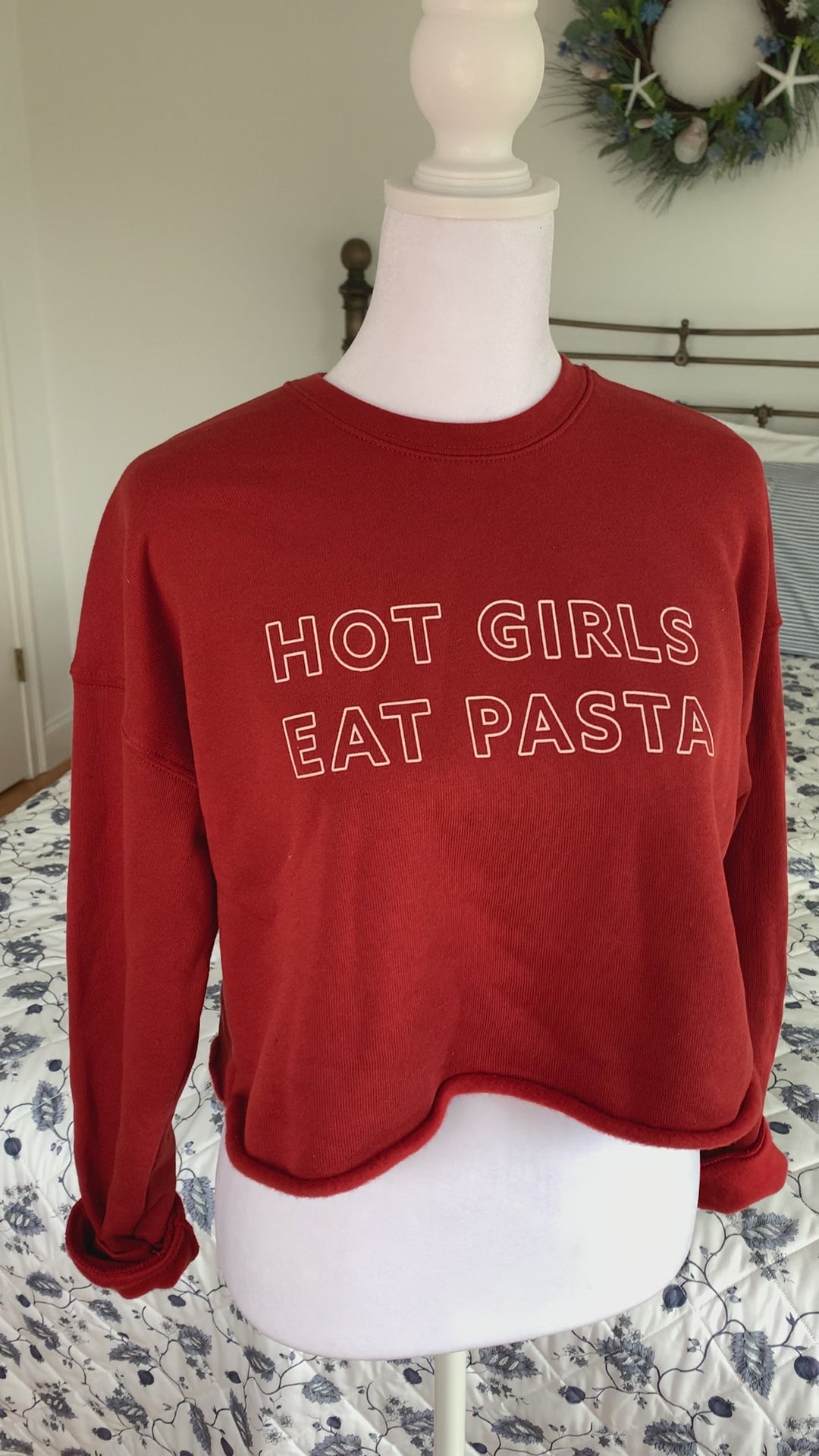 A red cropped sweatshirt that reads "Hot Girls Eat Pasta" hangs on a manikin 