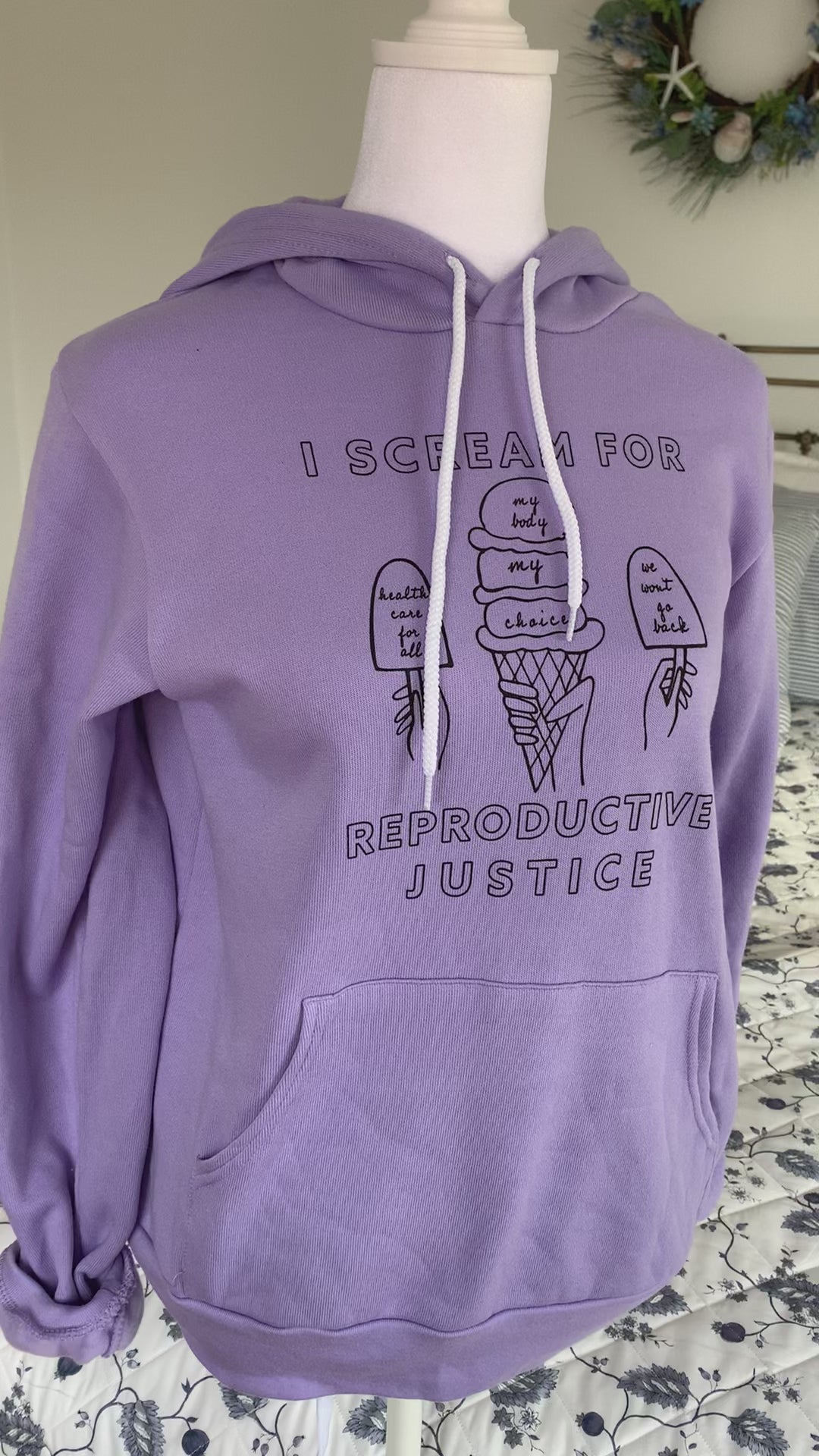 A lavender hoodie that reads "I scream for reproductive justice" hangs on a manikin
