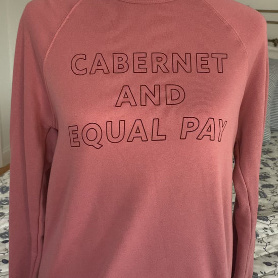 A mauve crewneck that reads "Cabernet and Equal Pay" hangs on a manikin 