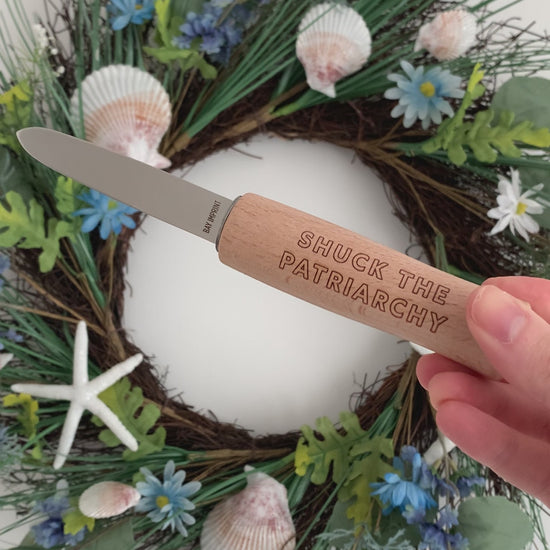 A woman holds an oyster shucker with an engraved handle that reads "Shuck the Patriarchy"