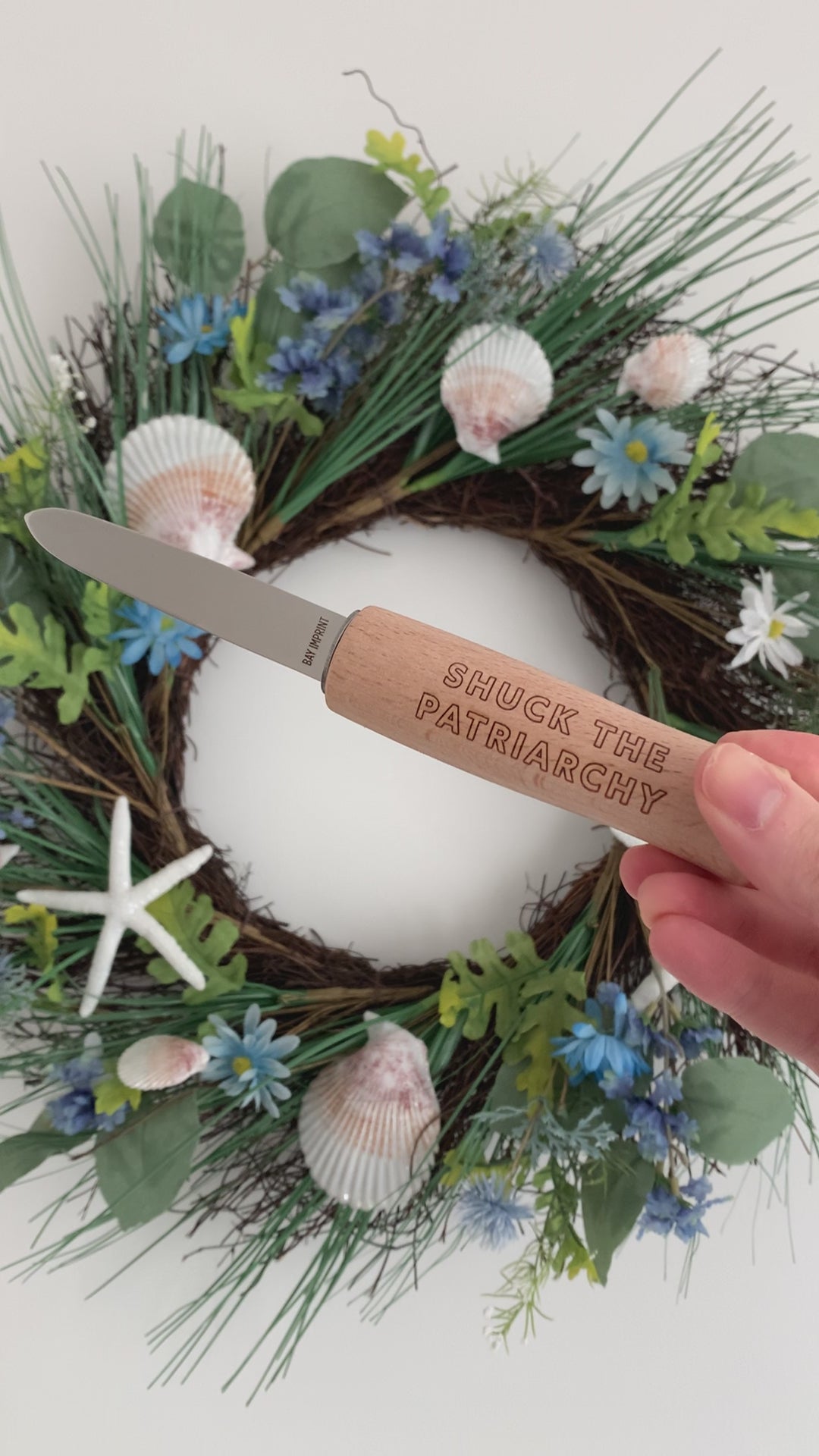 A woman holds an oyster shucker with an engraved handle that reads "Shuck the Patriarchy"