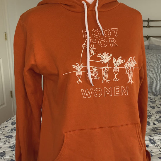 An orange hoodie that reads "Root for Women" hangs on a manikin