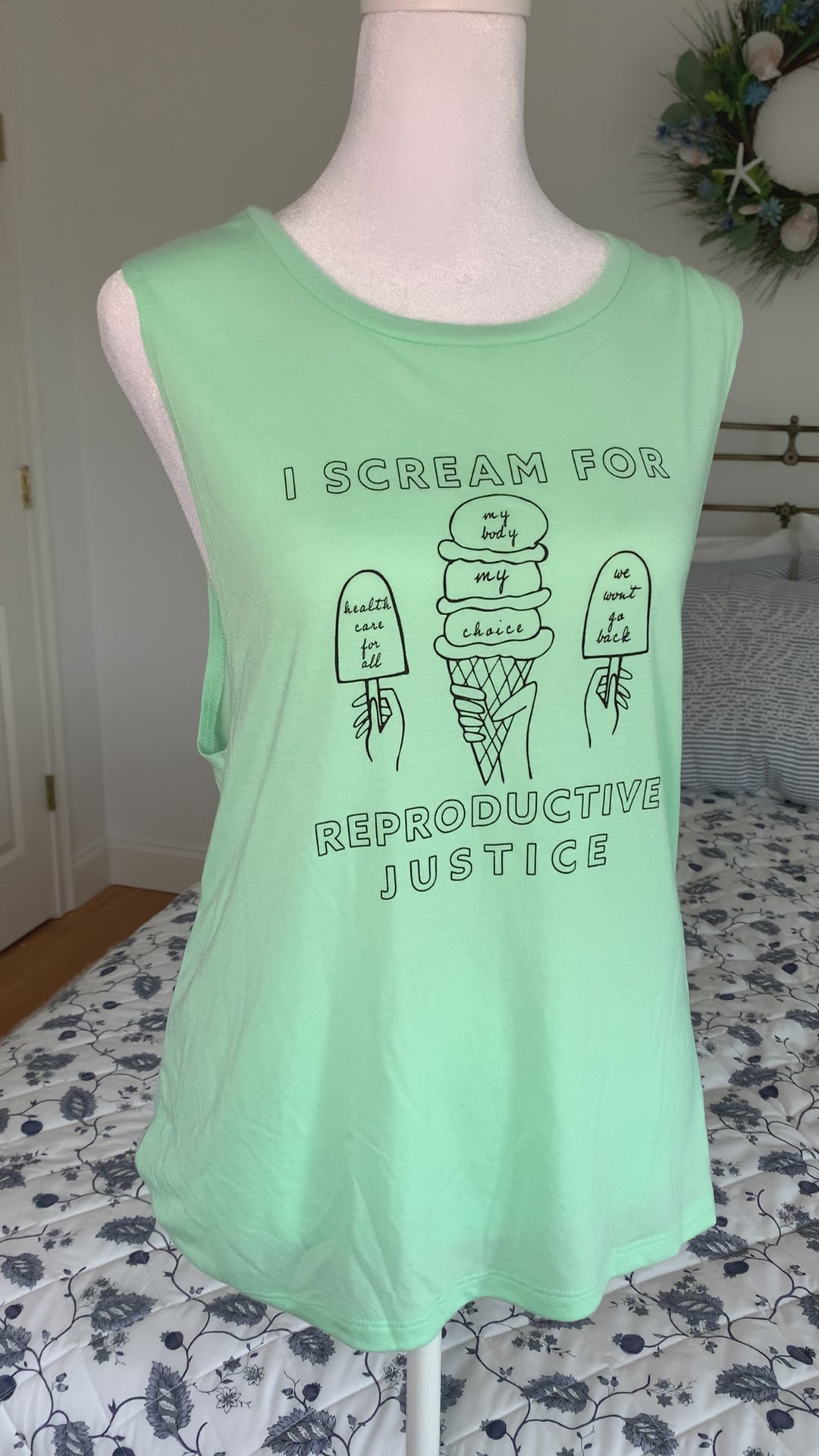 A mint green tank that reads "I scream for reproductive justice" hangs on a manikin 