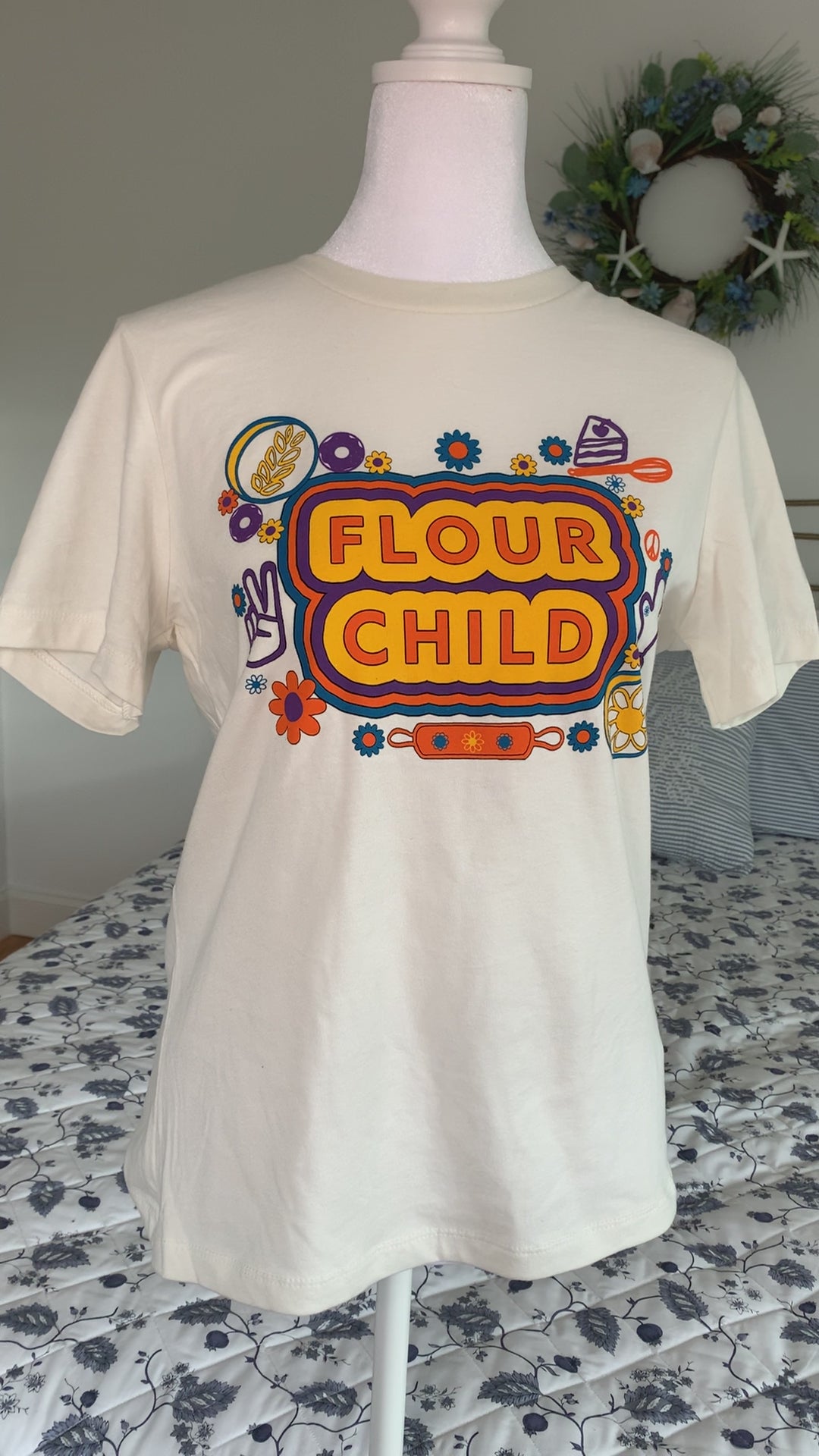 A white t-shirt that reads "Flour Child" with colorful designs hangs on a manikin