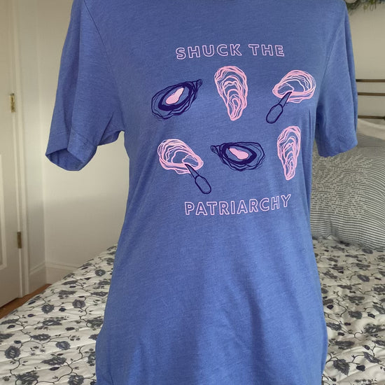 A bright blue tee that reads "Shuck the Patriarchy" in block letters hangs on a manikin
