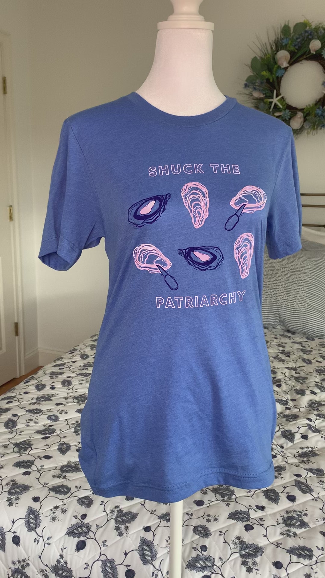 A bright blue tee that reads "Shuck the Patriarchy" in block letters hangs on a manikin