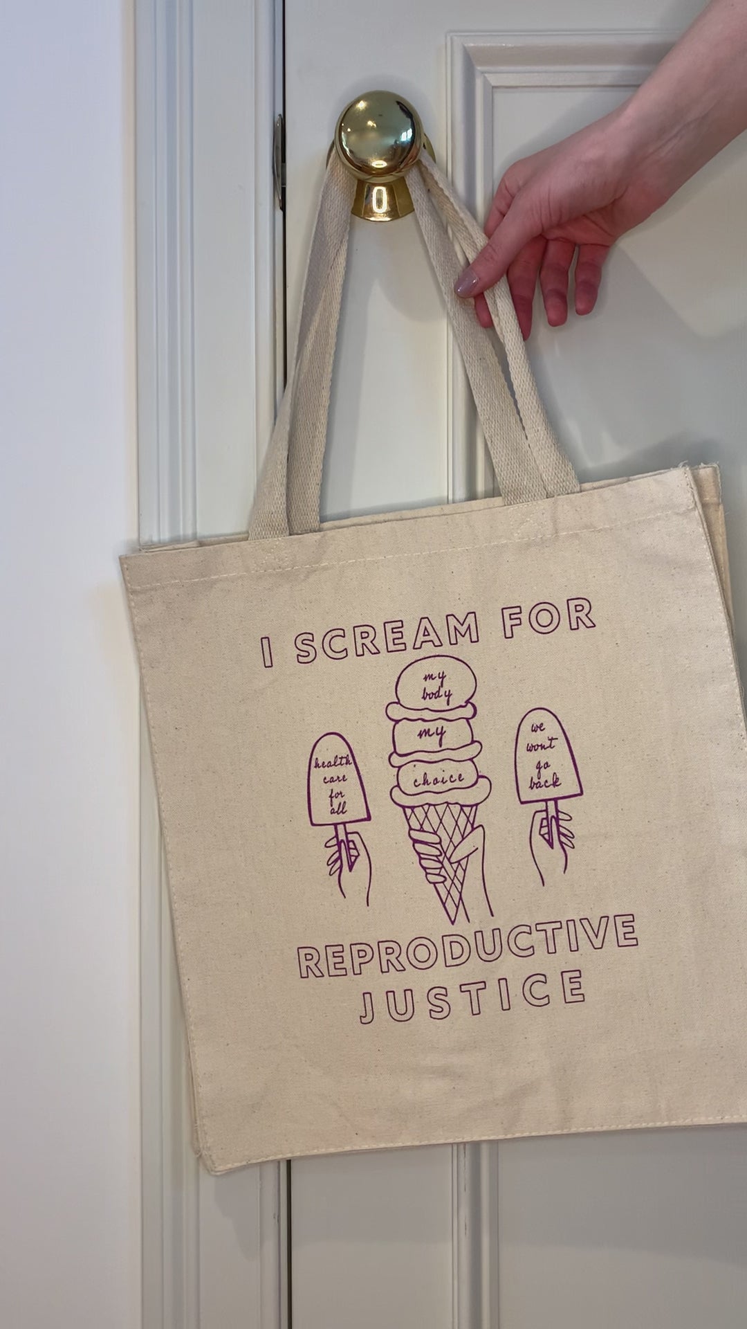 A canvas tote with raspberry block letters that reads "I scream for reproductive justice" hangs on a doorknob