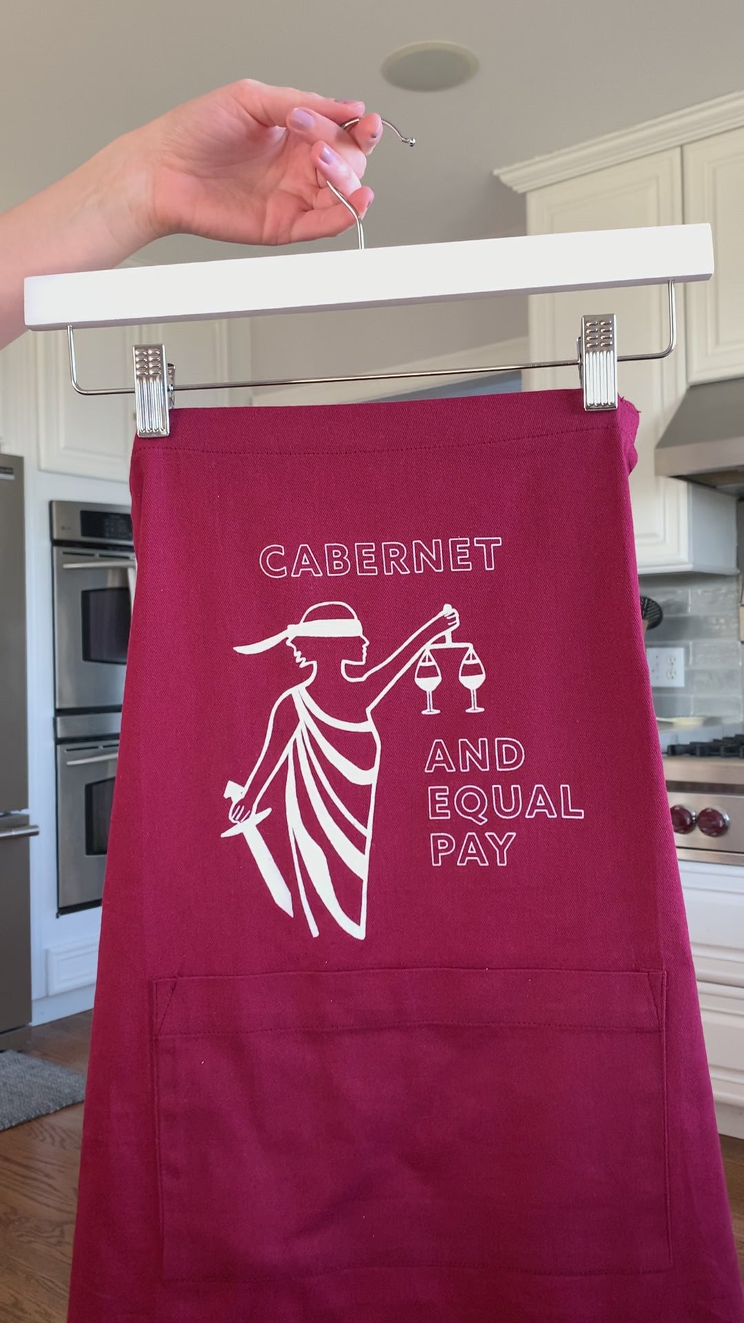 A red apron that reads "Cabernet and Equal Pay" hangs on a hanger