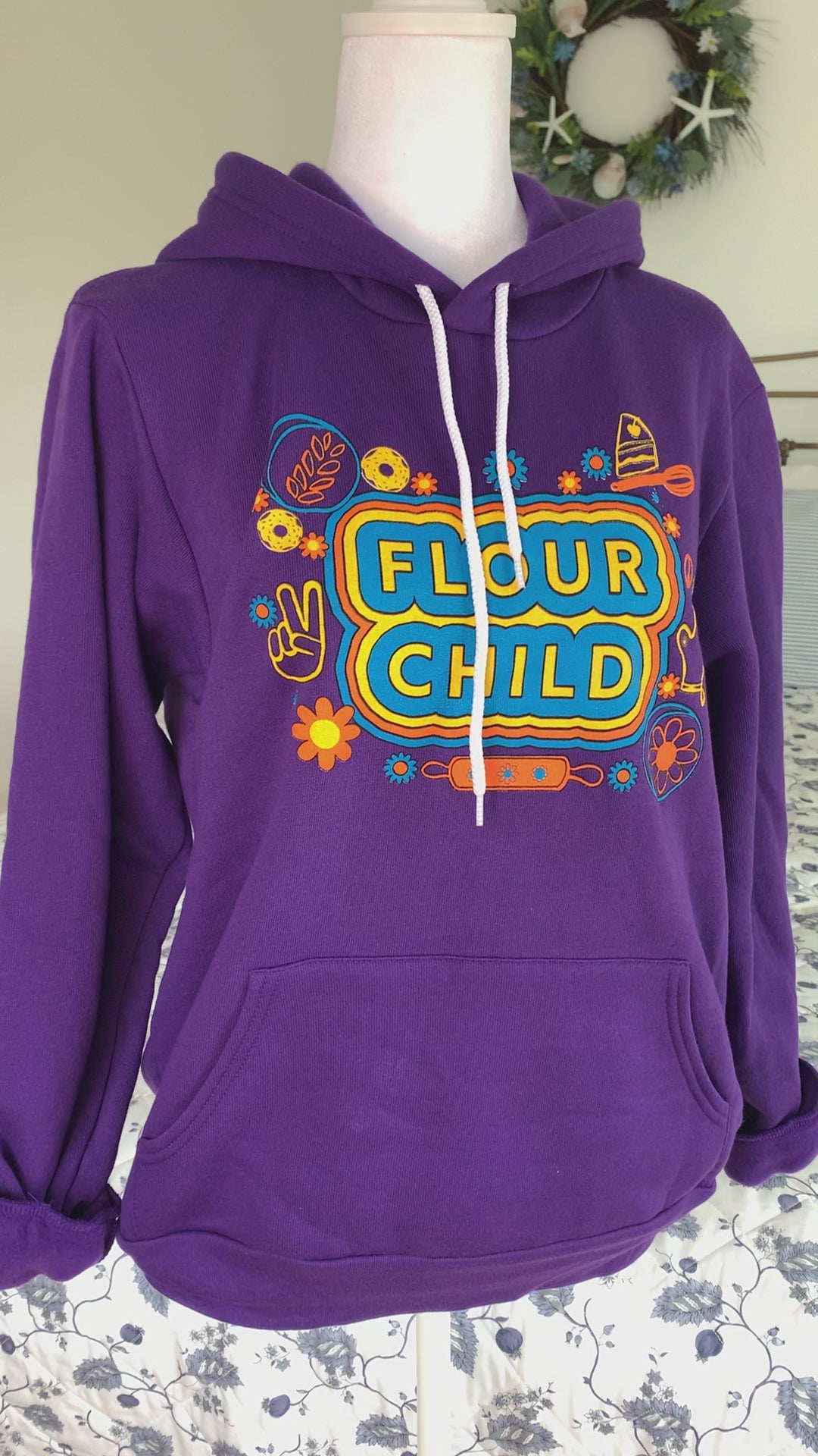 A purple hoodie that reads "Flour Child" hangs on a manikin 