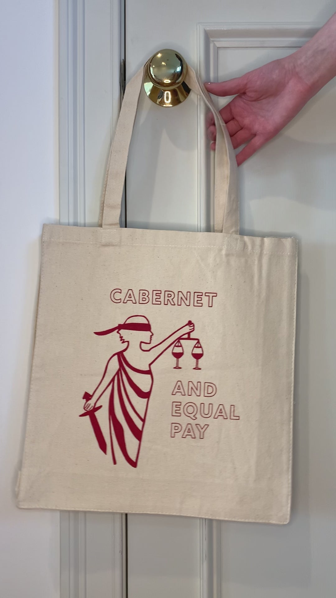 A canvas tote that reads "Cabernet and Equal Pay" hangs from a doorknob