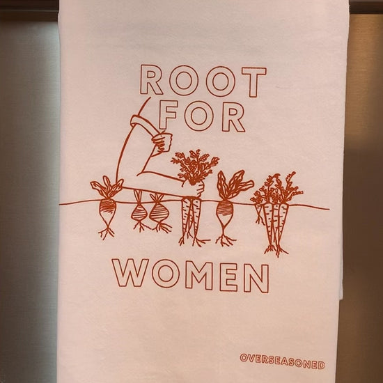 A white tea towel with orange block letters that read "Root for Women" hangs in a kitchen