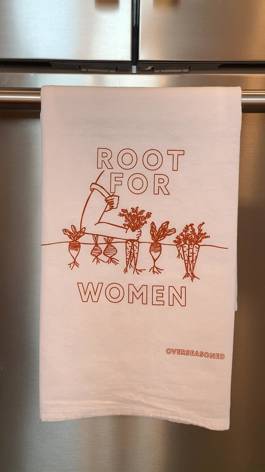 A white tea towel with orange block letters that read "Root for Women" hangs in a kitchen