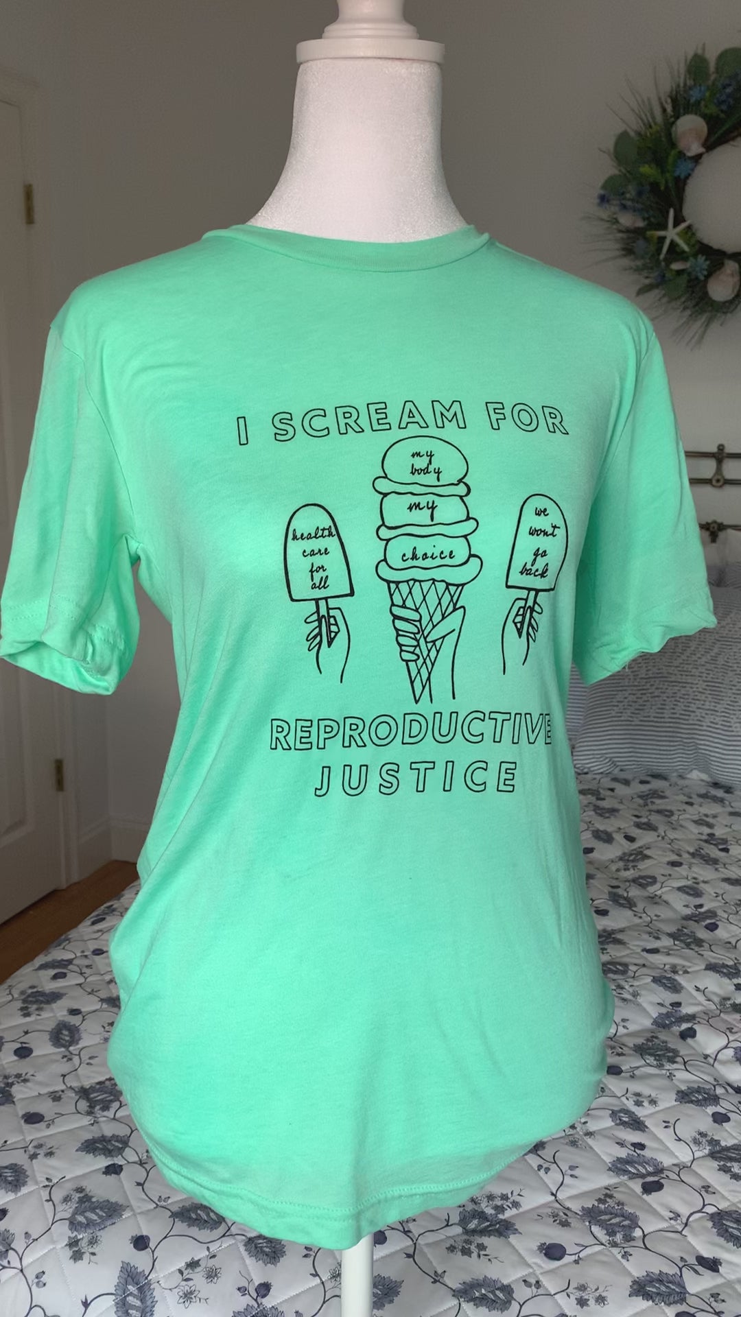 A mint green t-shirt that reads "I scream for reproductive justice" hangs on a manikin