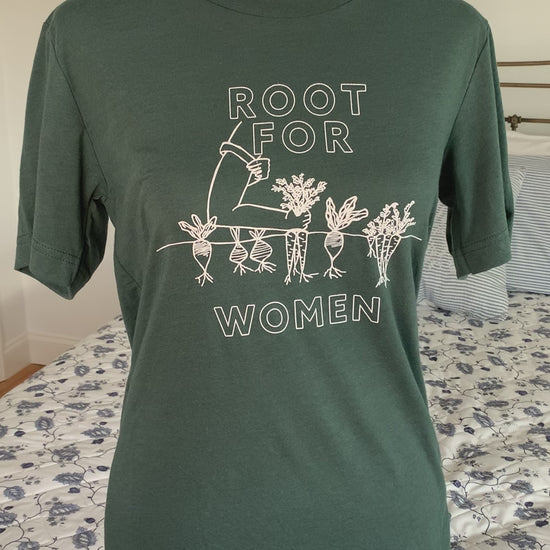 A green t-shirt that reads "Root for Women" with a garden illustration hangs on a manikin