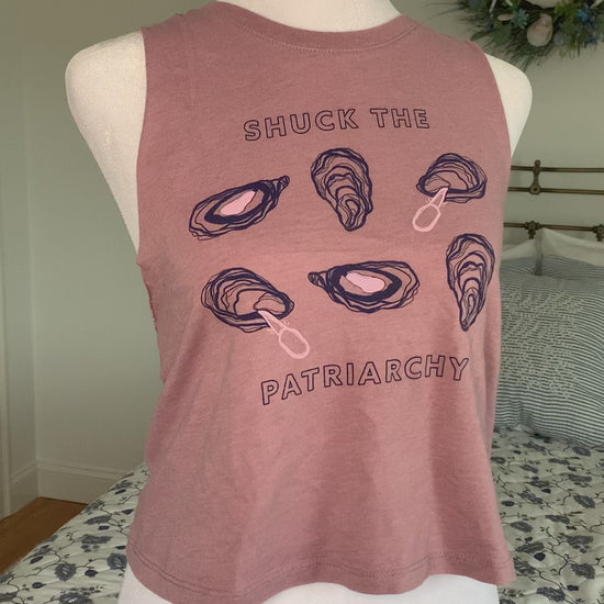 A cropped mauve tank that reads "Shuck the Patriarchy" hangs on a manikin