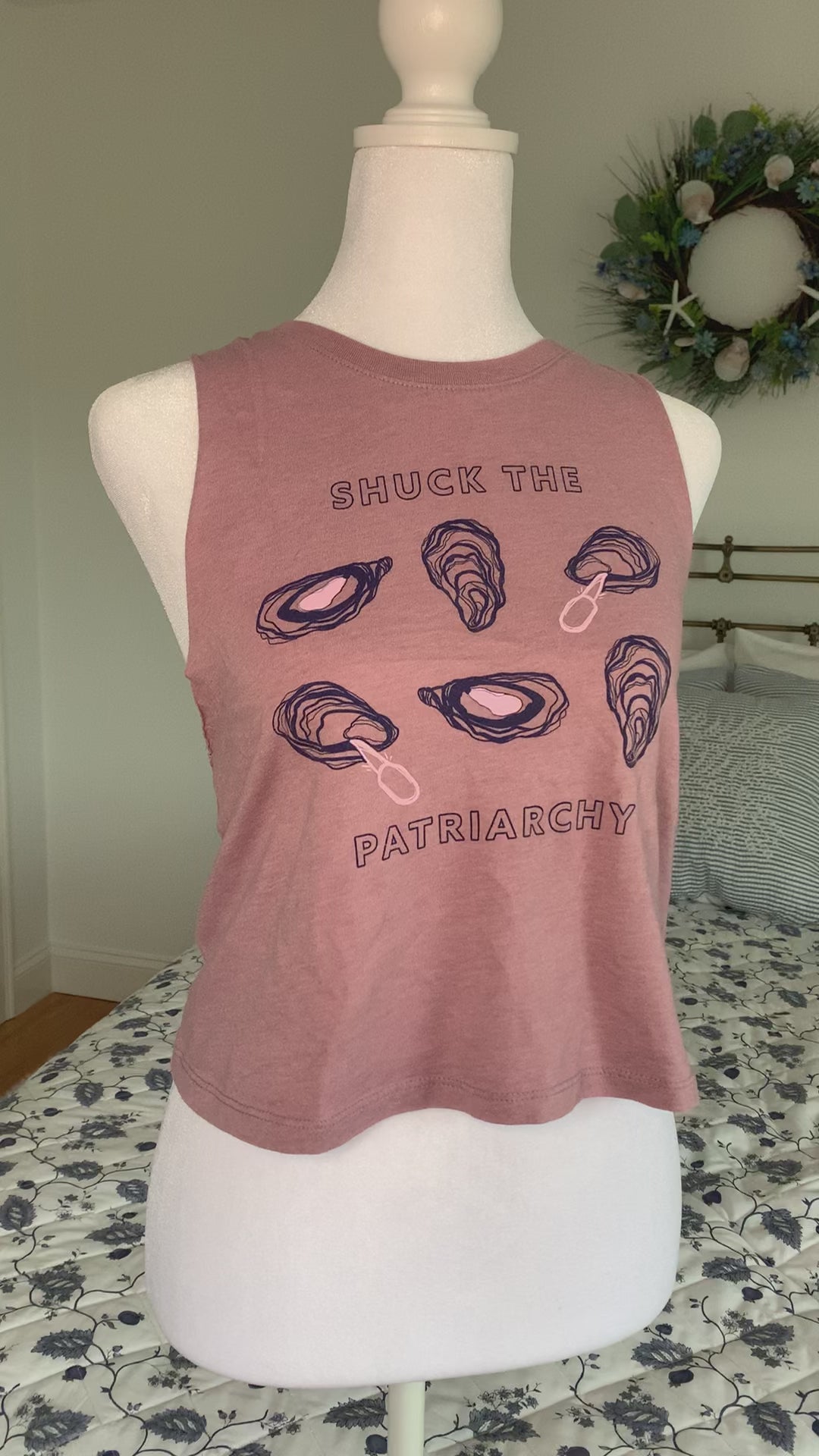 A cropped mauve tank that reads "Shuck the Patriarchy" hangs on a manikin