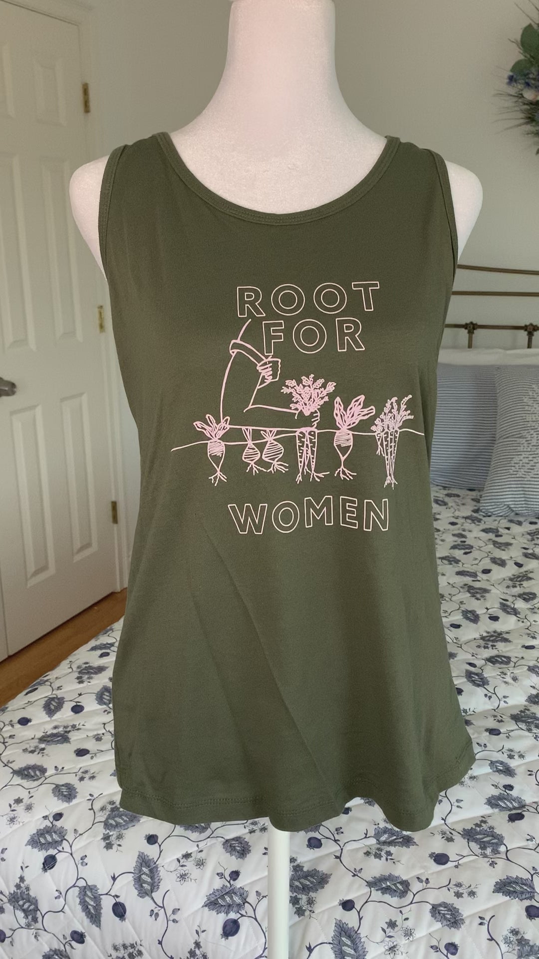 An olive green tank that reads "Root for Women" hangs on a manikin