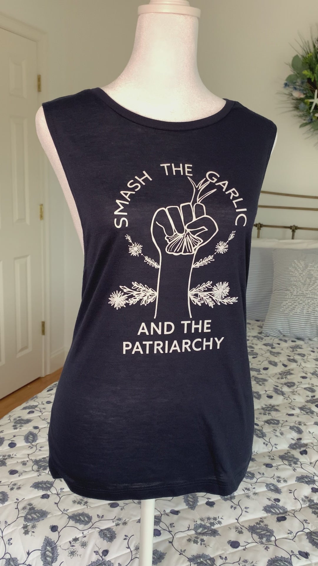 A navy tank with the words "Smash the Garlic and the Patriarchy" and a garlic illustration hangs on a manikin