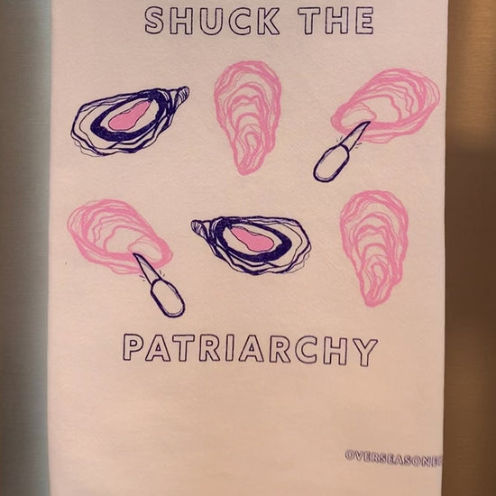 A white tea towel that reads "Shuck the Patriarchy" hangs in a kitchen