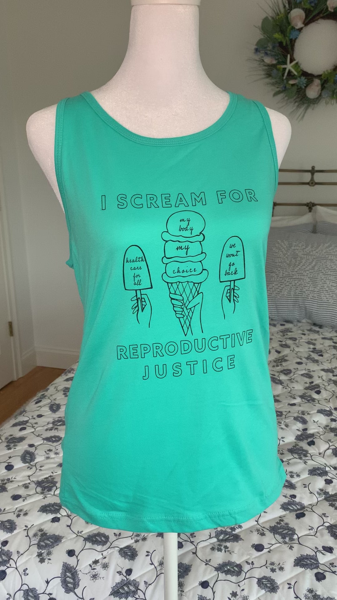 A teal tank top that reads "I scream for reproductive justice" hangs on a manikin