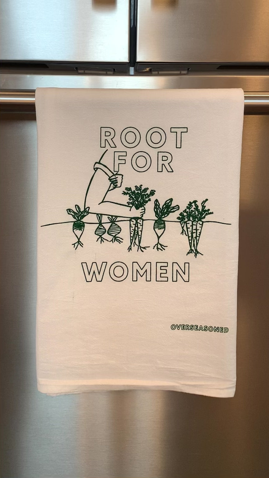 A white tea towel with "Root for Women" in green block letters hangs in a kitchen