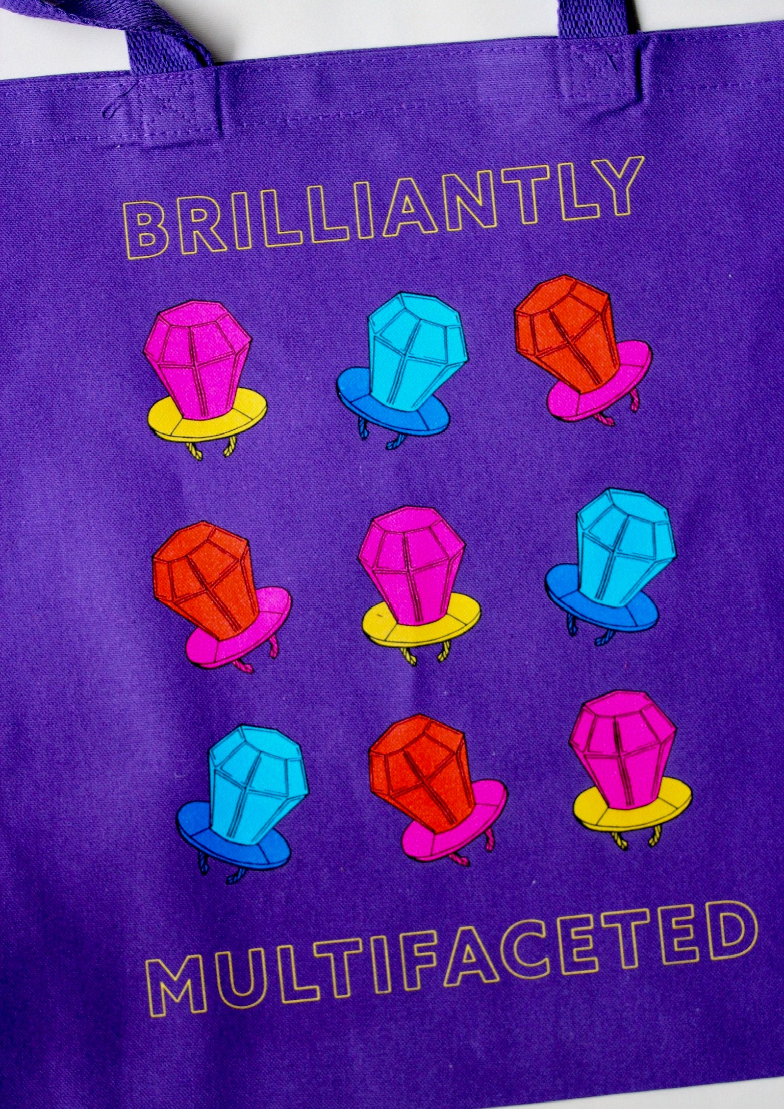 Purple tote bag with words "Brilliantly Multifaceted" and colored ring pop art