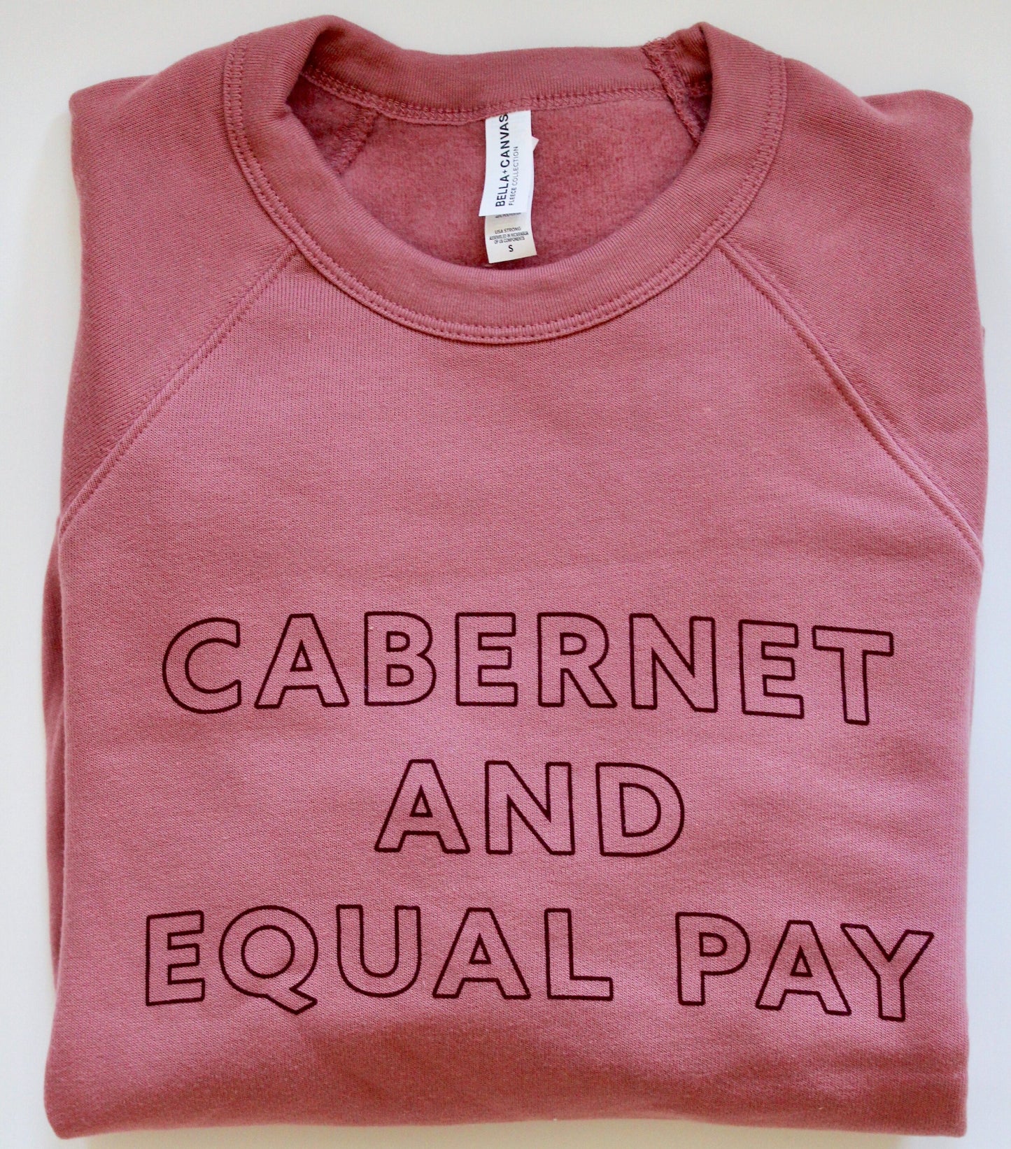 Pink crewneck sweatshirt with "Cabernet and Equal Pay" block writing