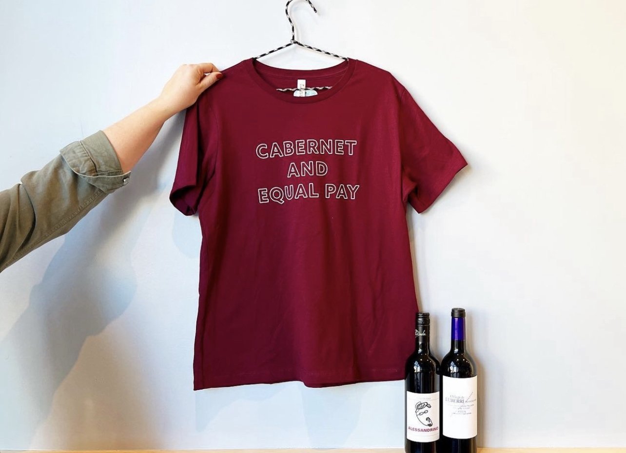 Cabernet colored t-shirt on a hanger held up with two bottles of wine