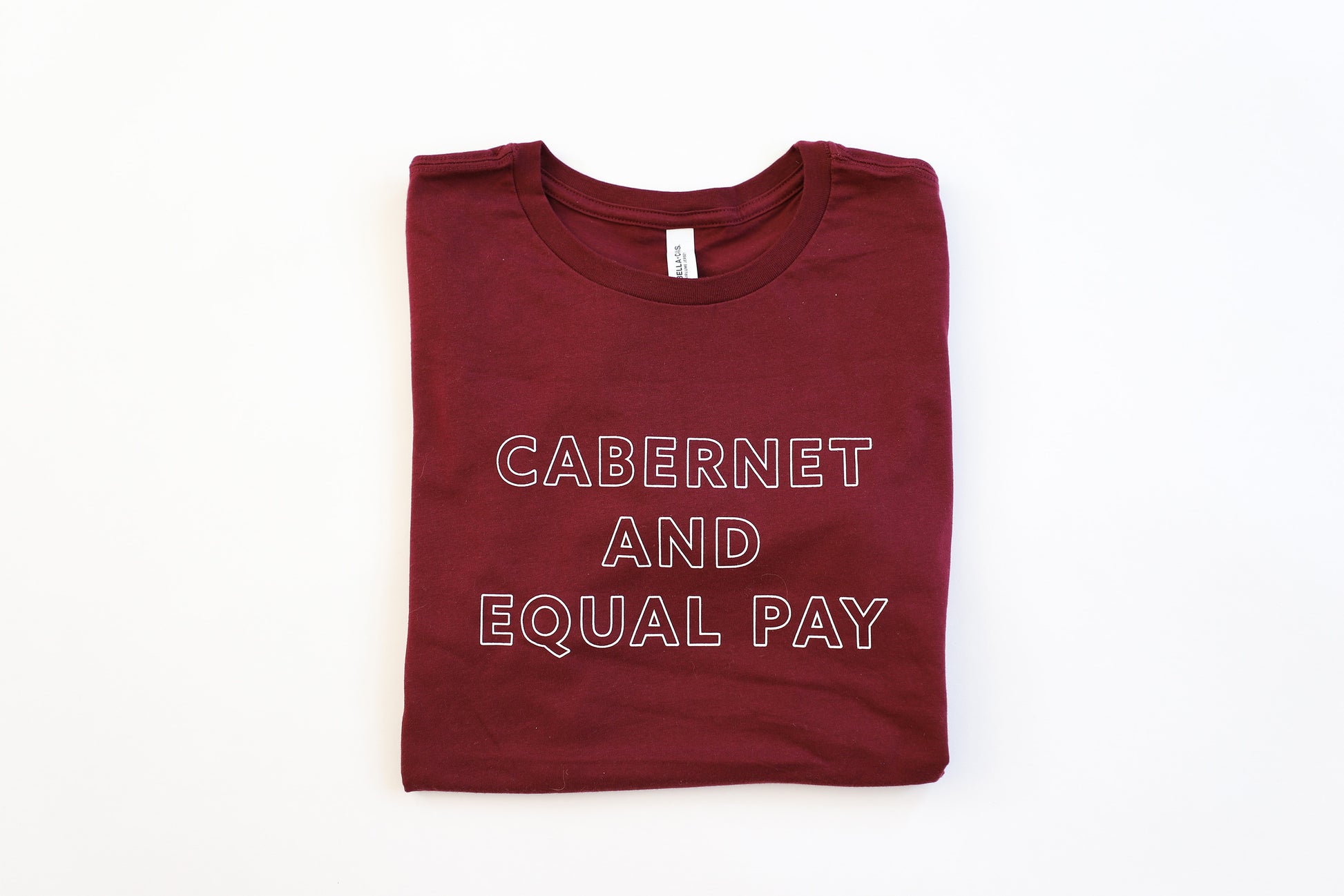 Cabernet colored tee folded with the white block letters that say "Cabernet and Equal Pay"