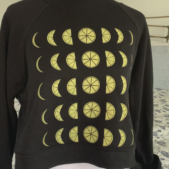 A black cropped sweatshirt with lemon moon phase design hangs on a manikin