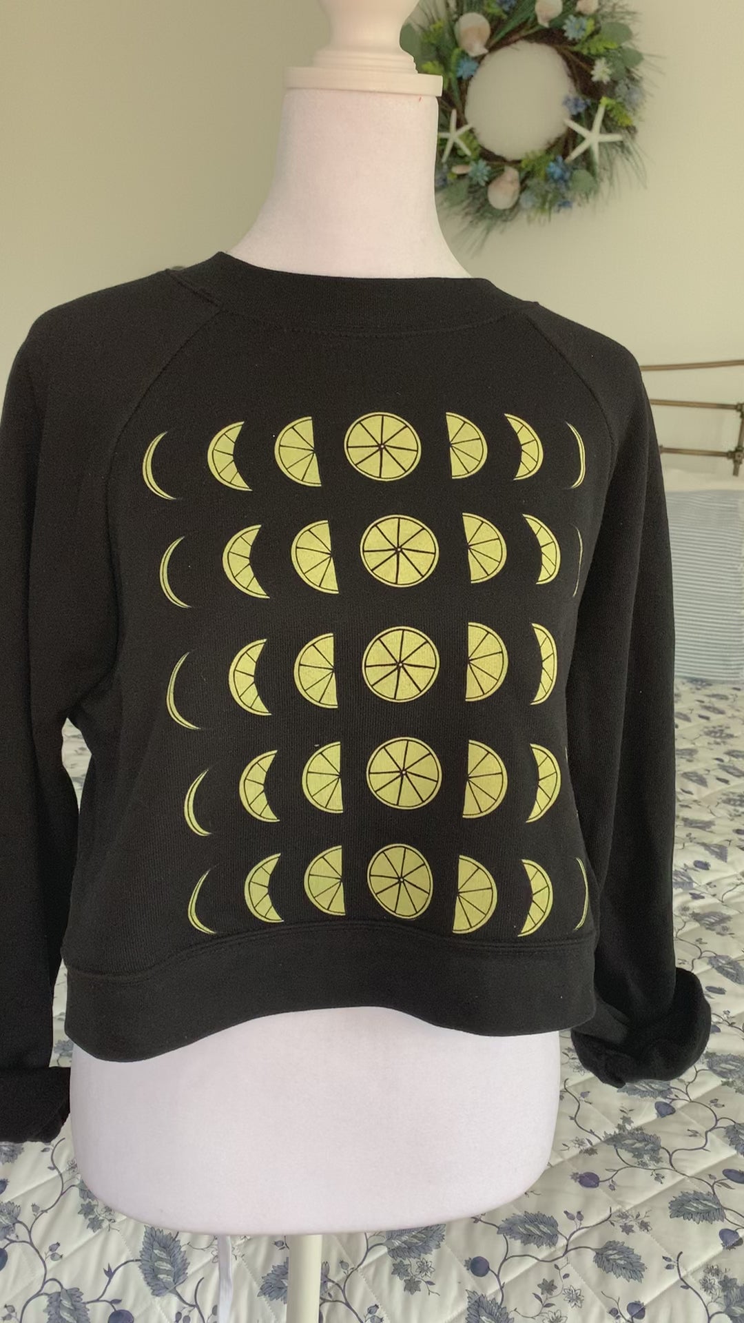A black cropped sweatshirt with lemon moon phase design hangs on a manikin