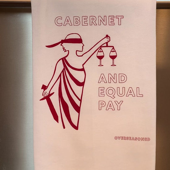 A white tea towel that reads "Cabernet and Equal Pay" in red lettering hangs from a bar