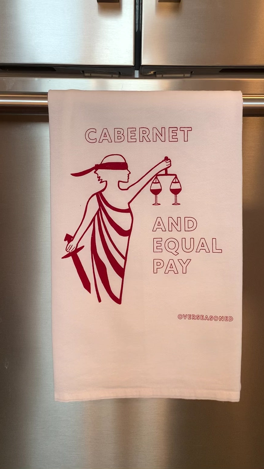 A white tea towel that reads "Cabernet and Equal Pay" in red lettering hangs from a bar