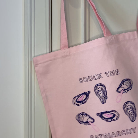 A pink tote that reads "Shuck the Patriarchy" hangs on a doorknob