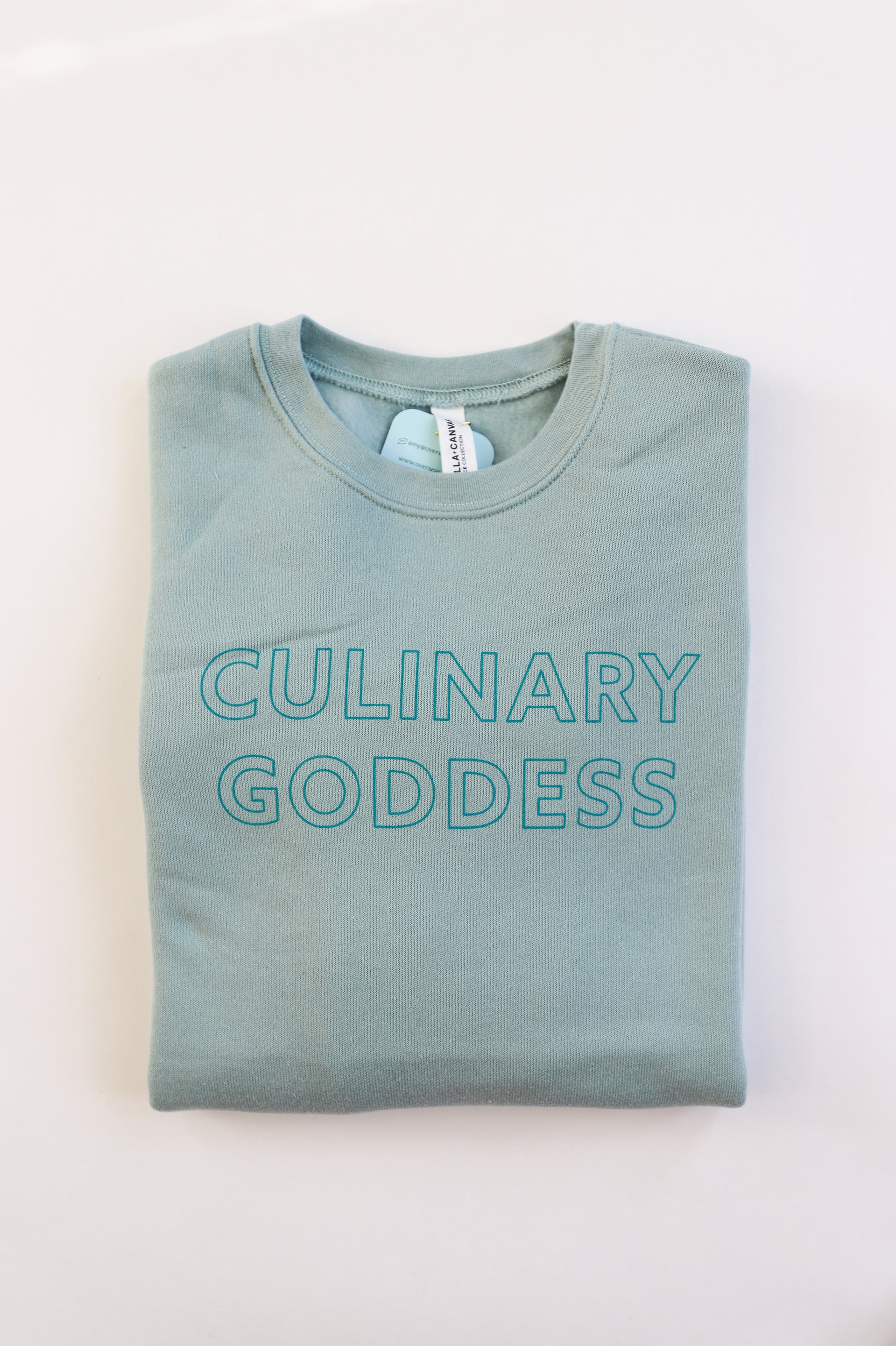 Folded dusty blue crewneck with "Culinary Goddess" in teal block lettering