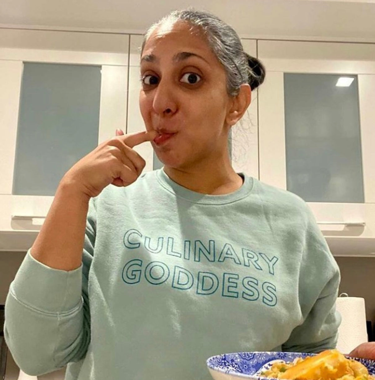 Woman tasting food in a blue Culinary Goddess crewneck