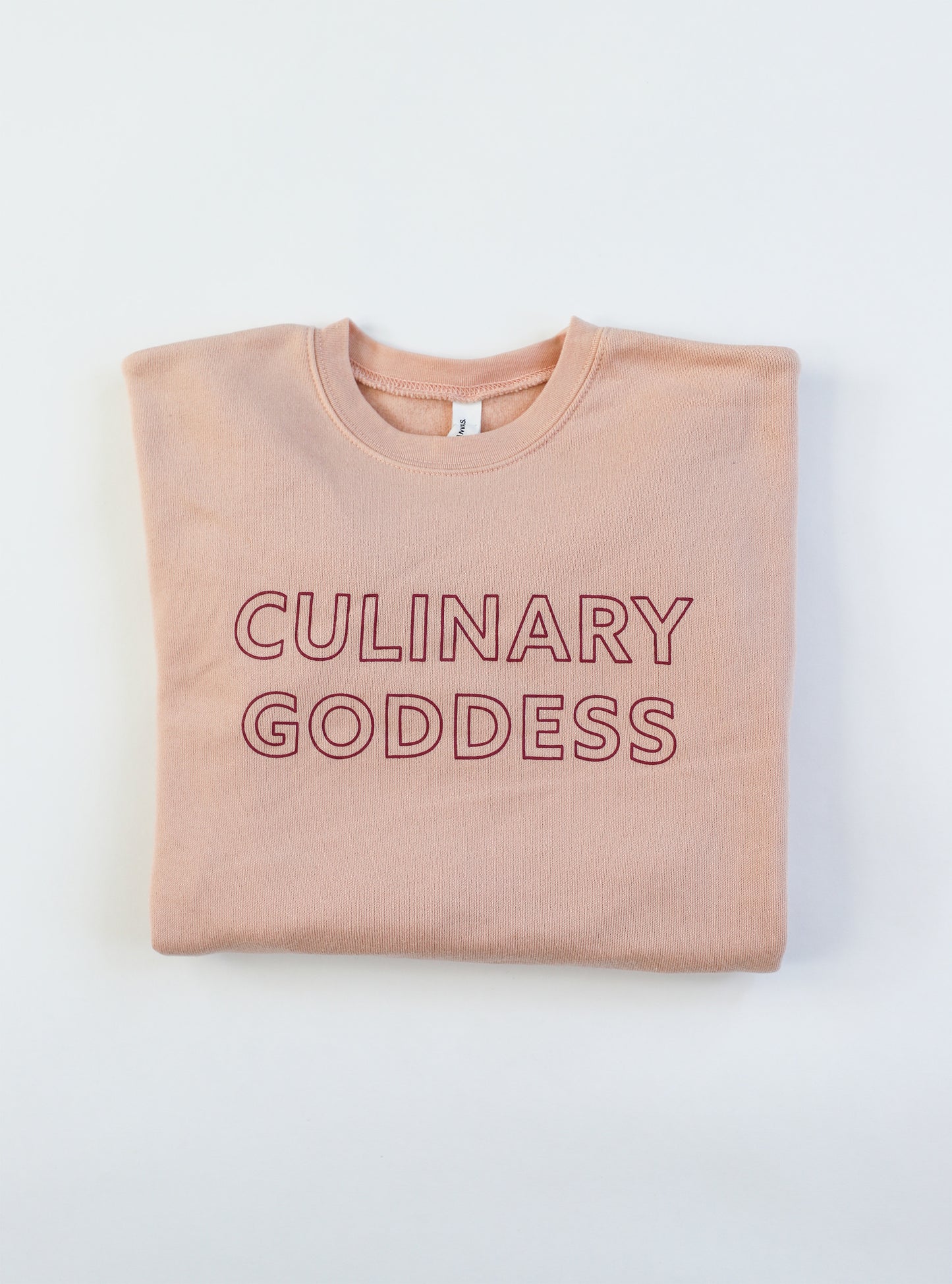 Folded pink crewneck sweatshirt with the words "Culinary Goddess"