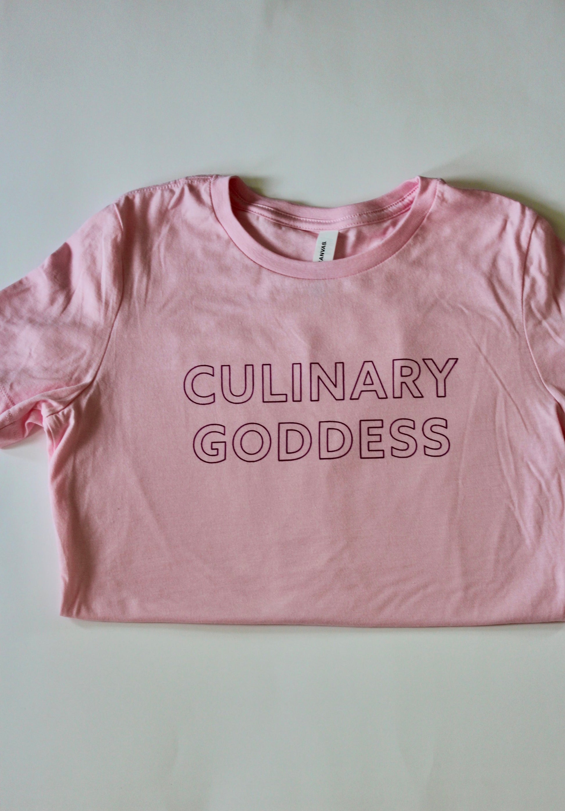 Pink tee with raspberry block letters that read "Culinary Goddess"