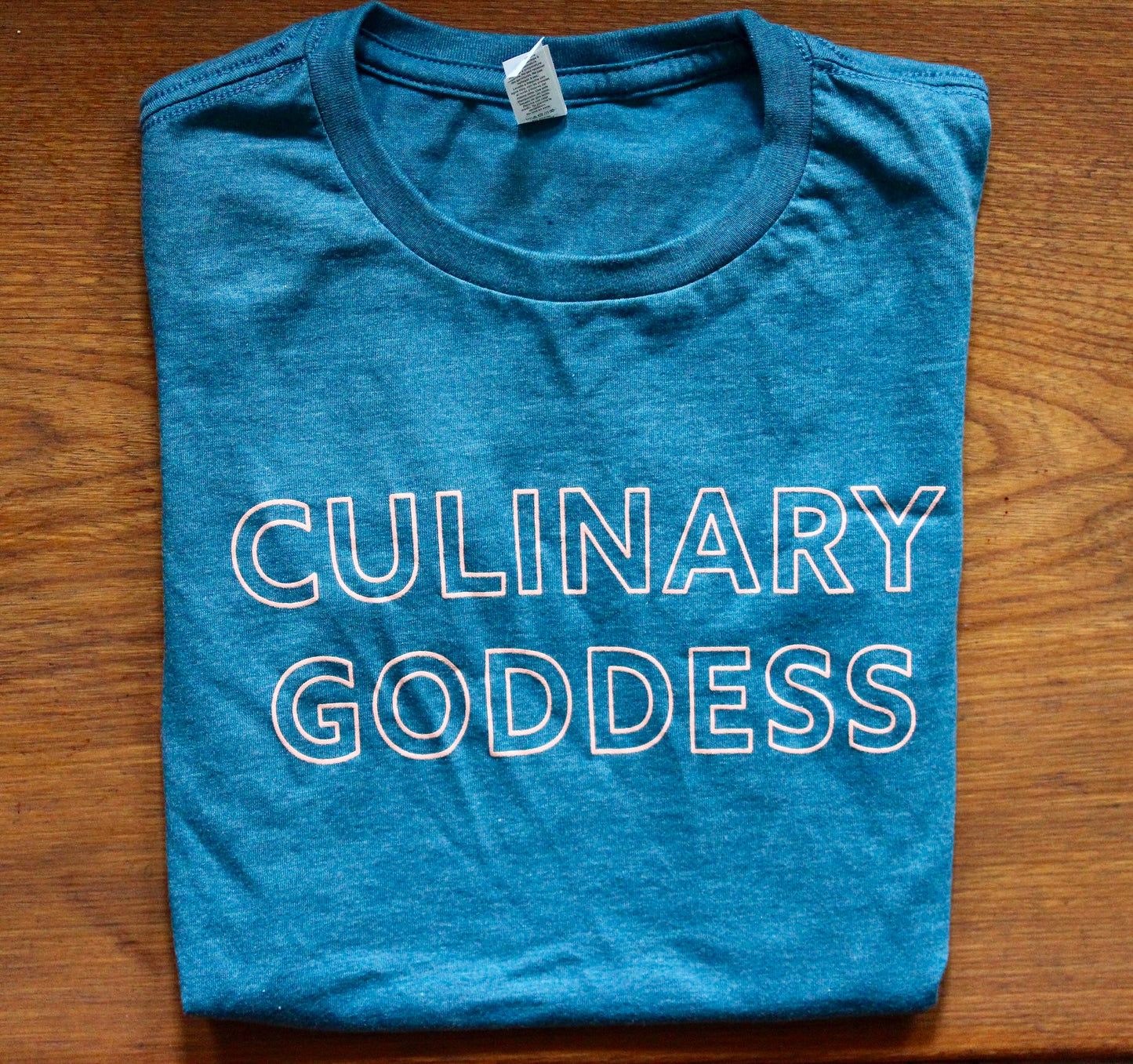 Teal folded tea with pink block letters that say "Culinary Goddess"