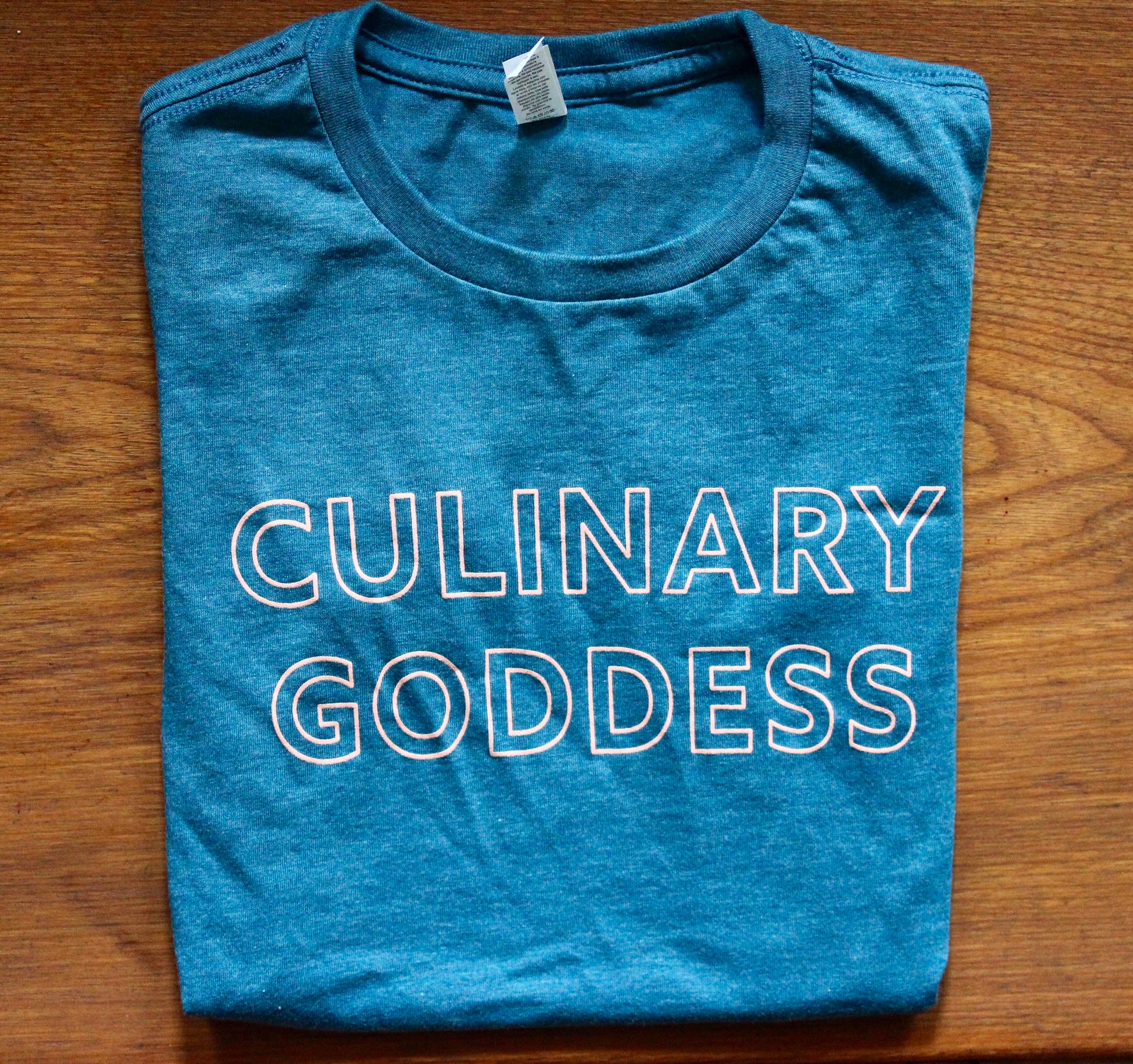 Teal folded tea with pink block letters that say "Culinary Goddess"
