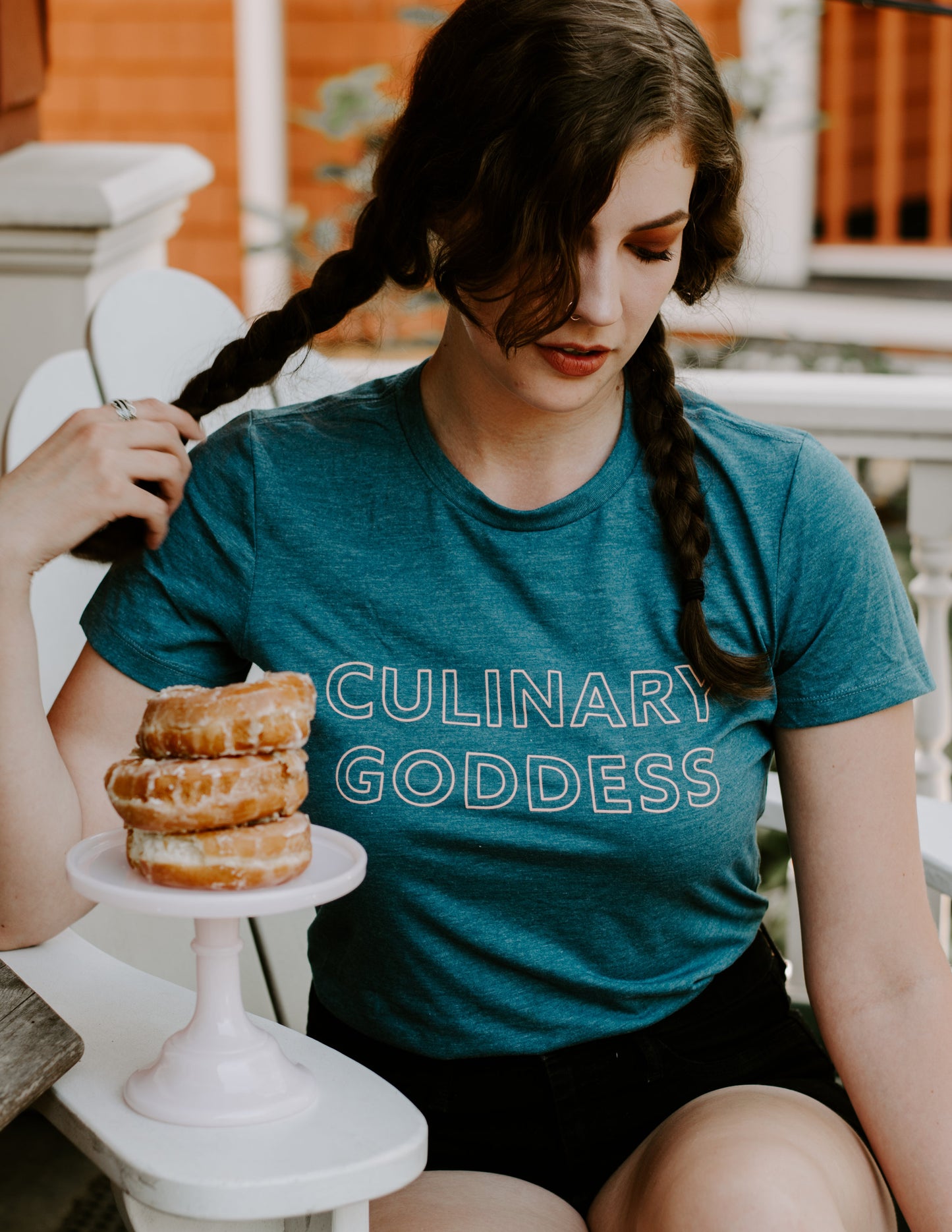 A woman wearing a teal Culinary Goddess tee with a plate of donuts