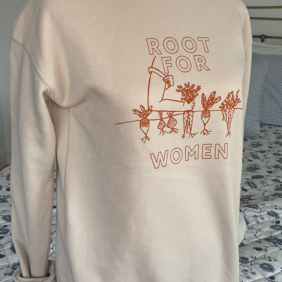 A natural color sweatshirt that reads "Root for Women" hangs on a manikin