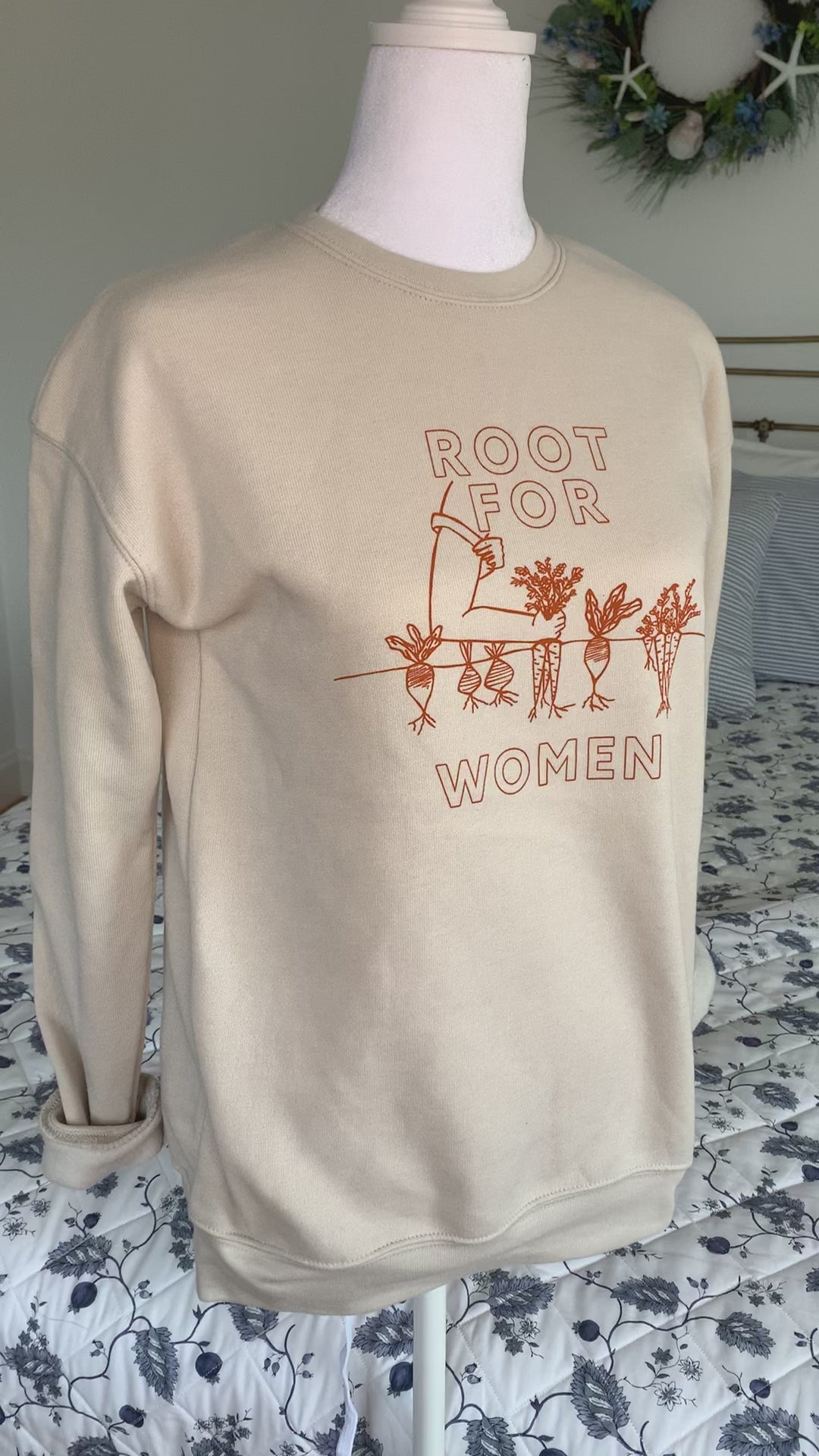 A natural color sweatshirt that reads "Root for Women" hangs on a manikin