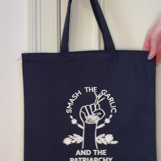 A navy blue tote that reads "Smash the Garlic and the Patriarchy" hangs on a doorknob