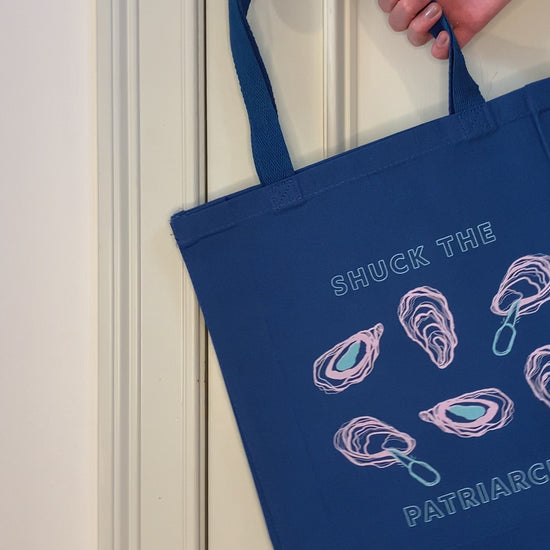 A blue tote that reads "Shuck the Patriarchy" hangs on a doorknob