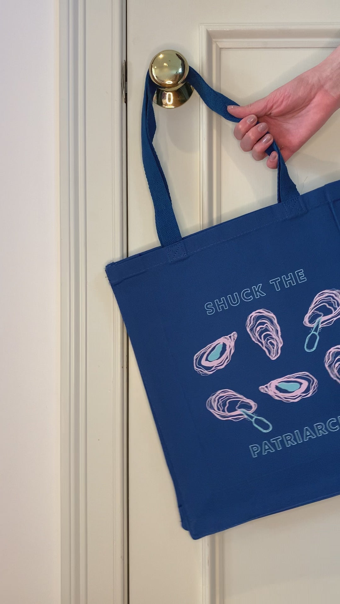 A blue tote that reads "Shuck the Patriarchy" hangs on a doorknob