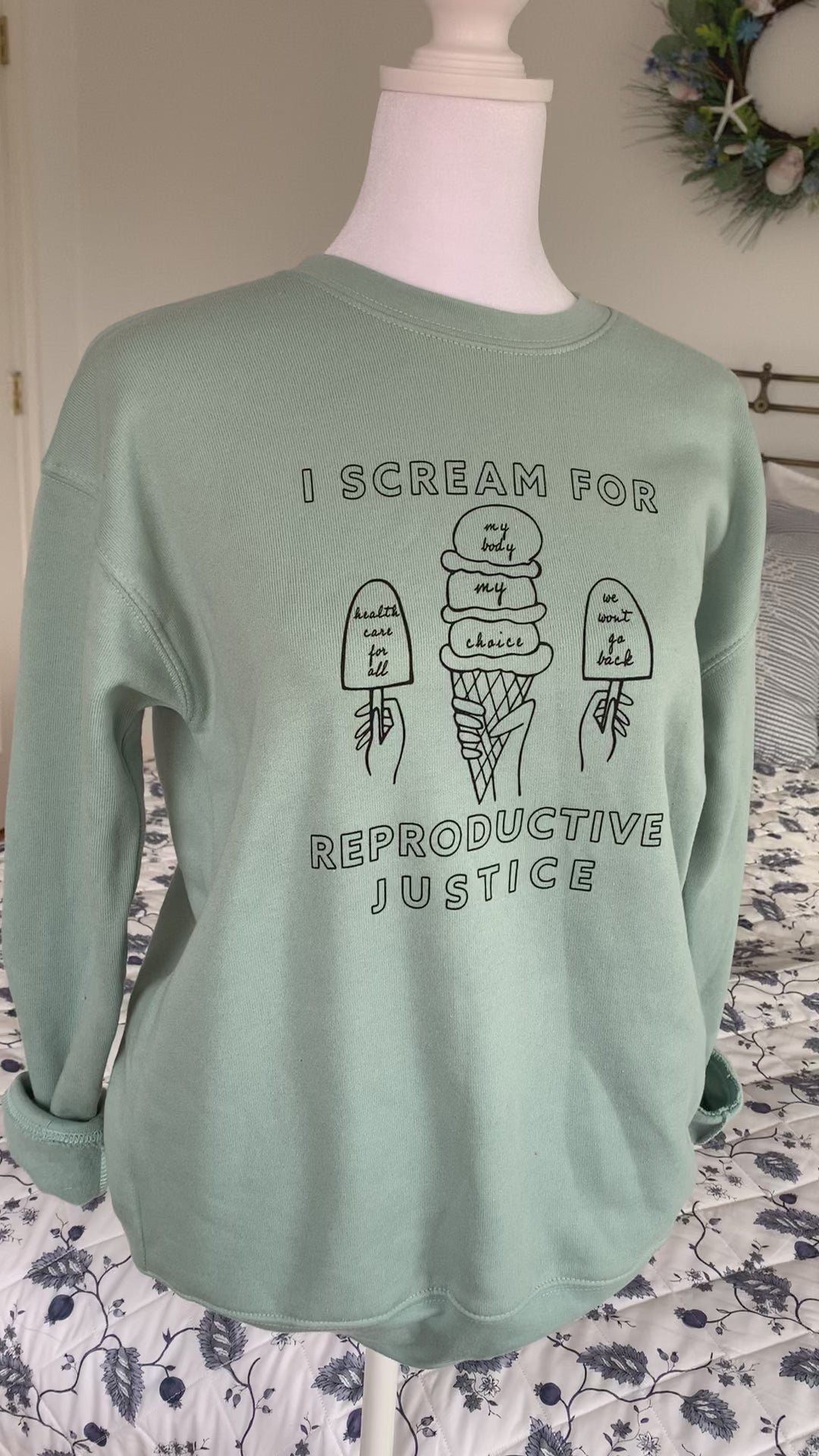 A dusty blue crewneck sweatshirt that reads "I scream for reproductive justice" hangs on a manikin
