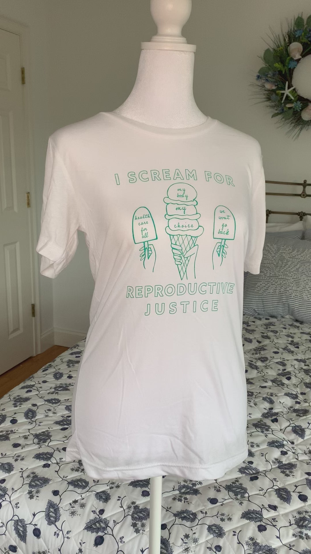 A white t-shirt that reads "I scream for reproductive justice" hangs on a manikin